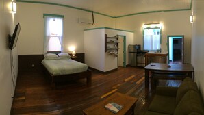 A small, cozy room with a bed, a table, a chair, and a kitchenette.