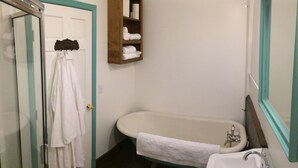 A bathroom with a bathtub, a sink, a wooden shelf with towels, and a glass shower enclosure.