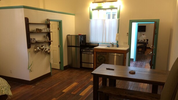 A compact kitchen with a refrigerator, stove, and sink. A dining table and a sofa are in the living area.