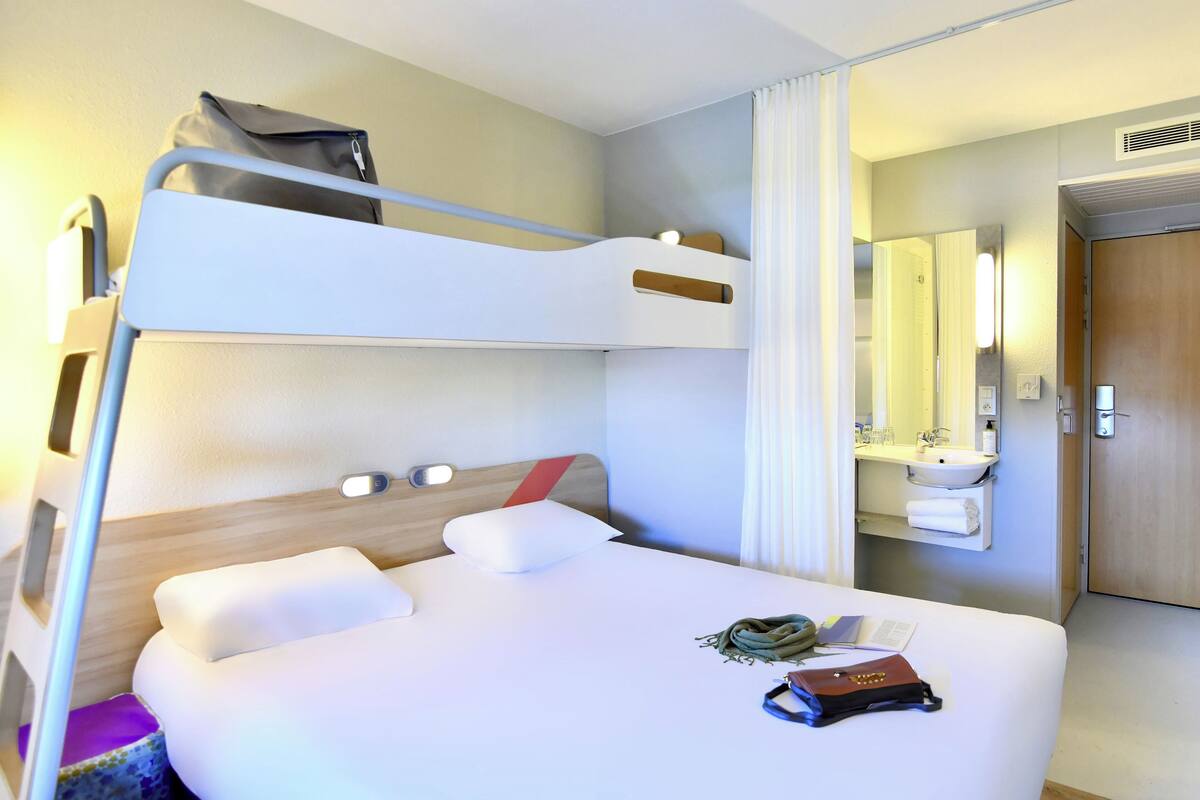 A bunk bed with a headboard, a bedside table with a book, and a suitcase on the upper bunk.