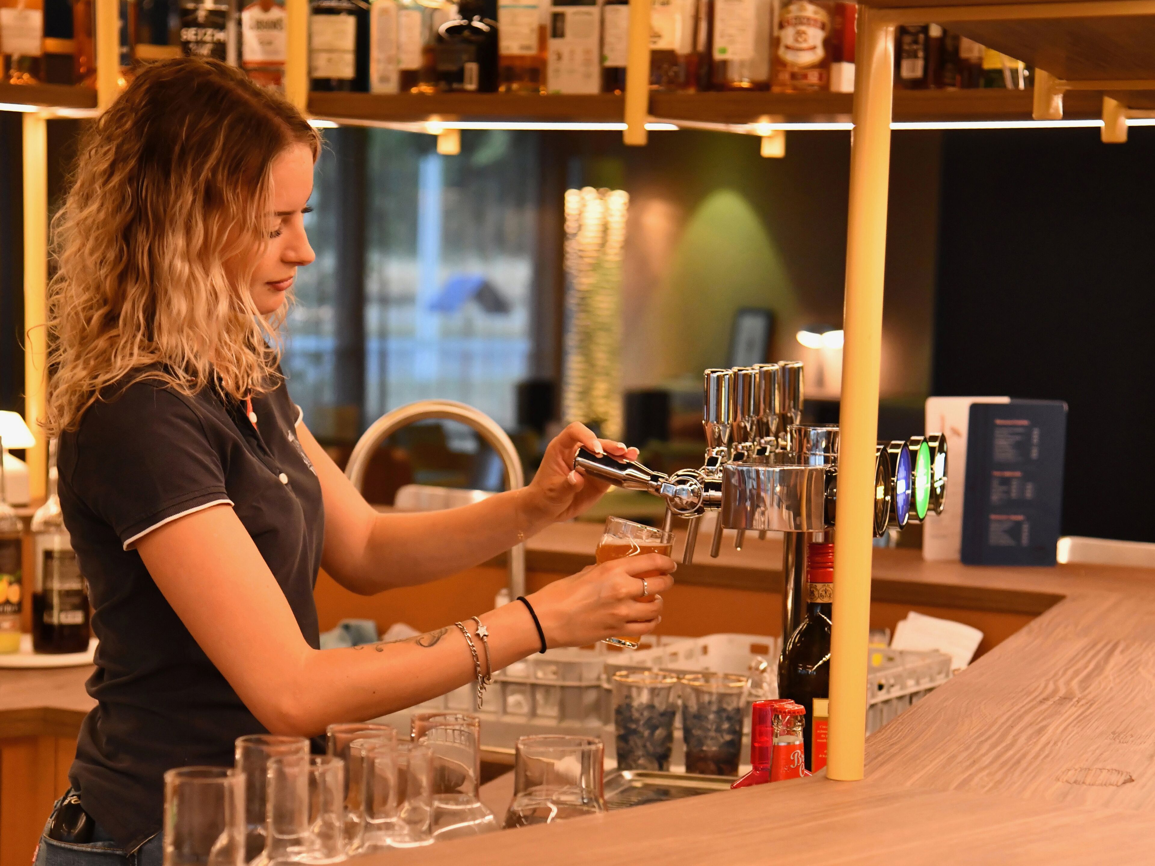 Una persona usando una máquina de café en un bar, con varios vasos y botellas al fondo.