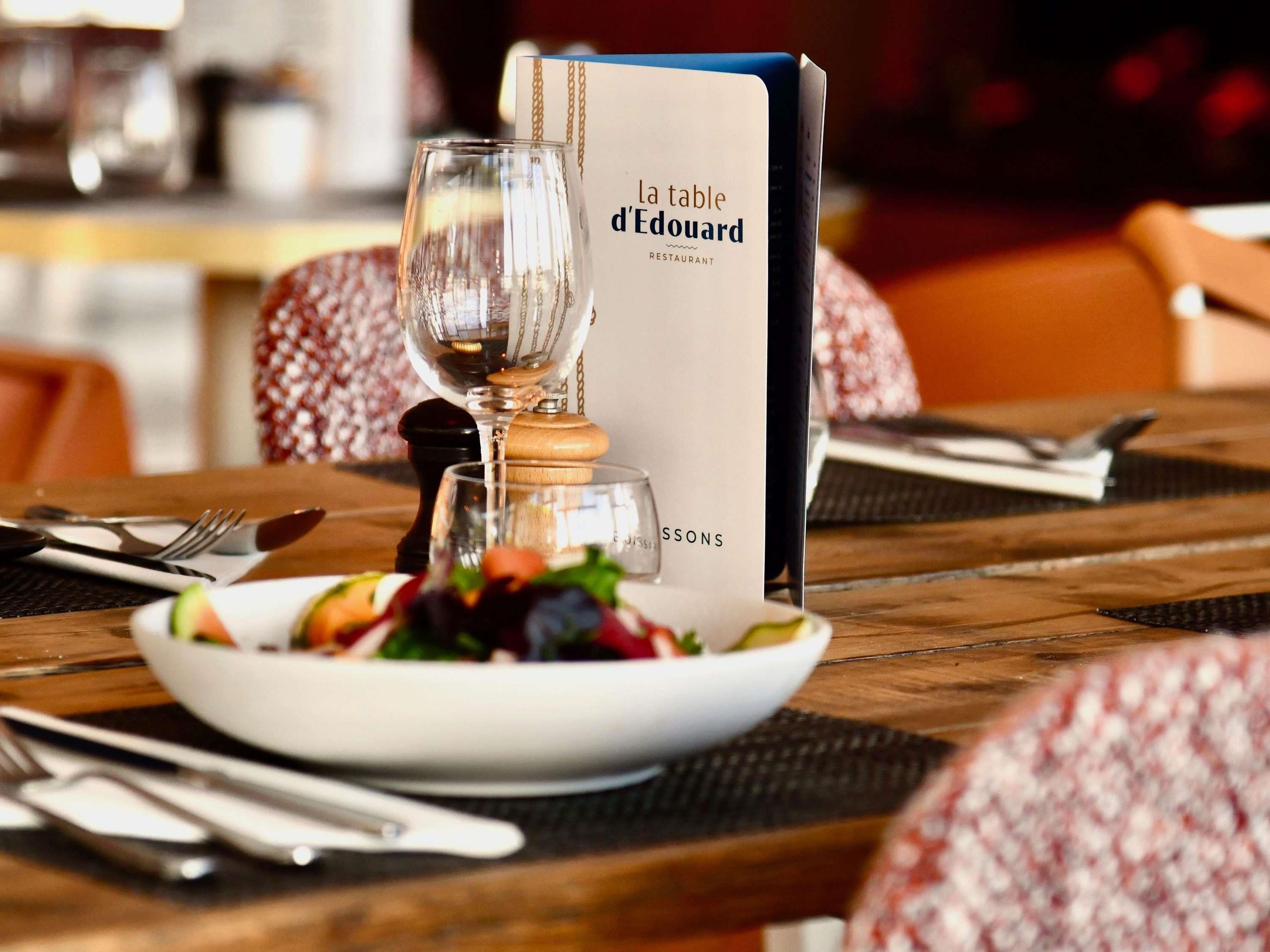 Une table de restaurant avec un présentoir à menus, une carafe à vin en verre et une assiette de salade.