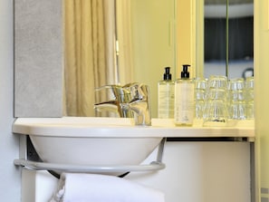 A bathroom with a white sink, a mirror, and a shelf with toiletries. - ibis budget Nantes Rezé Aéroport (Reze)