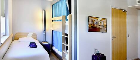 A hotel room with a bed, a bedside table, a suitcase, a bunk bed, and a door.