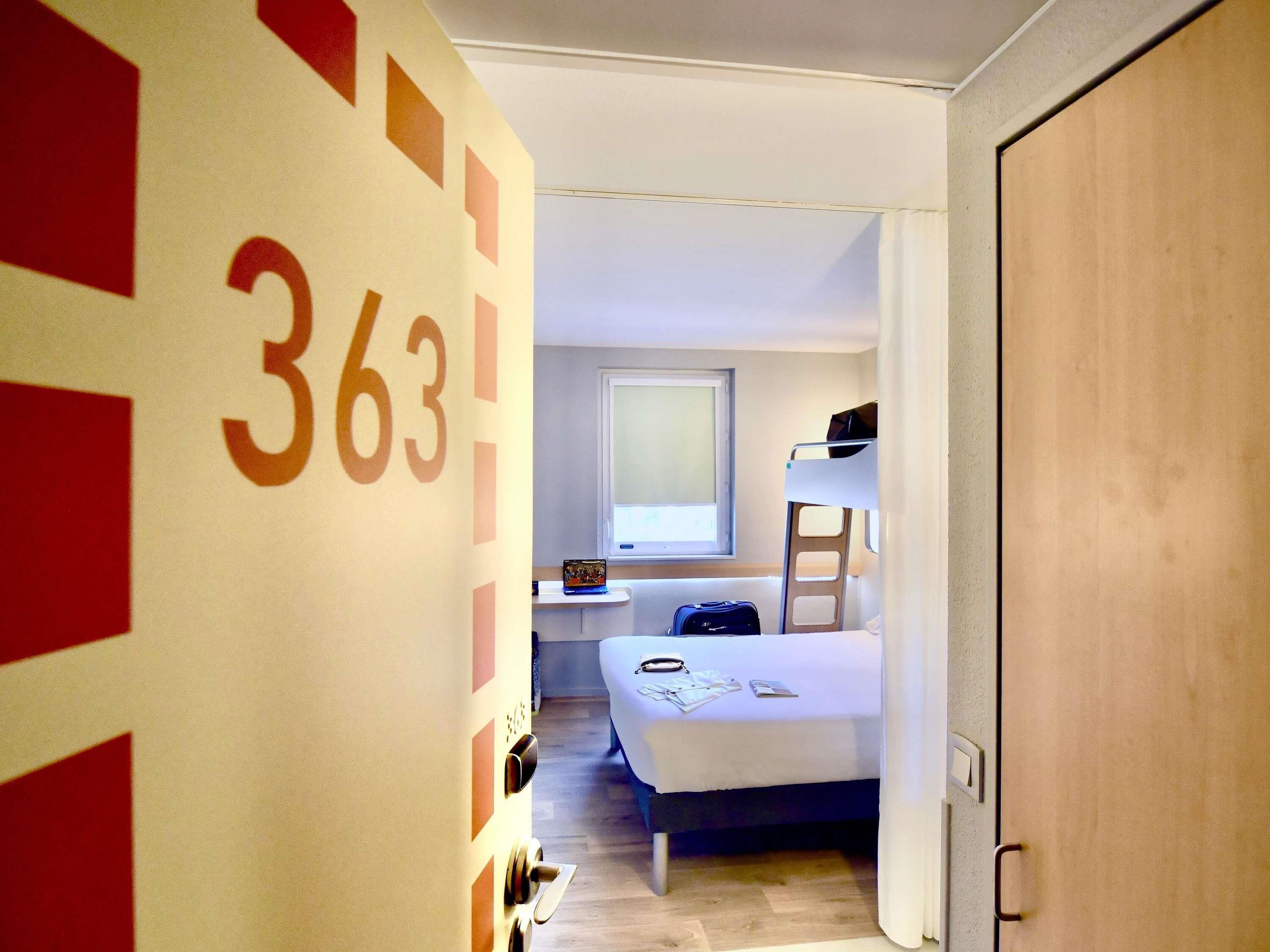 Una habitación de hotel con literas, una mesita de noche con lámpara y una ventana.