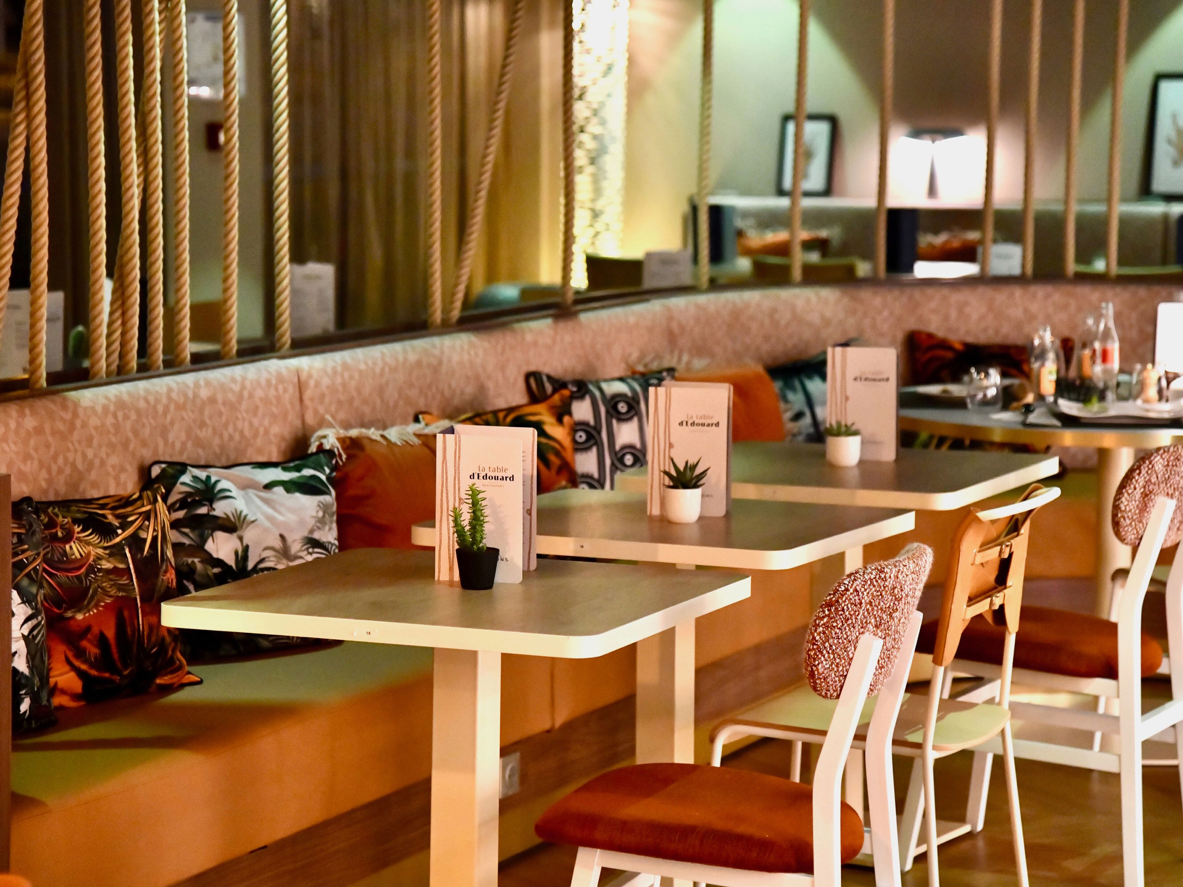 A restaurant with a long counter, cushioned seating, and small potted plants.
