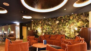 A modern lounge area with orange upholstered seating, a round table, and a wall adorned with a dense floral mural.