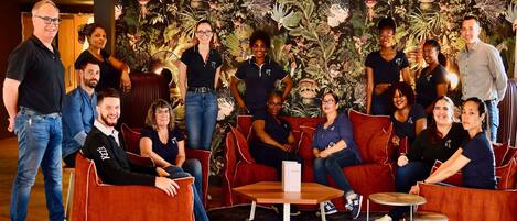 Un grupo de personas en un moderno salón con una pared de temática tropical, asientos rojos y una pequeña mesa redonda.