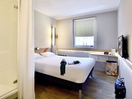 Une chambre d’hôtel avec un lit, une fenêtre, un bureau, une télévision et un espace pour les bagages.