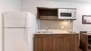 A compact kitchen with a white refrigerator, a microwave, and wooden cabinets. - Extended Stay America Suites - Norco (Norco)