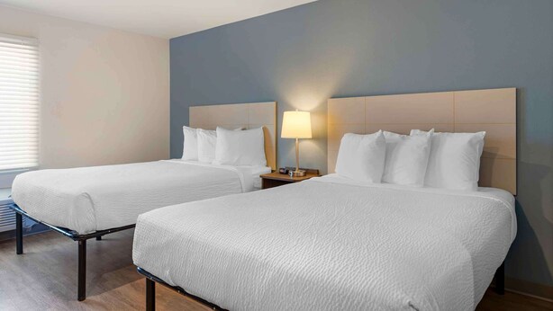 A hotel room with two beds, a nightstand with a lamp, and a window with blinds. - Extended Stay America Suites - Norco (Norco)
