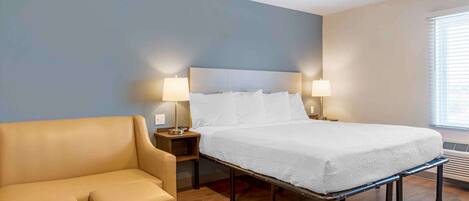 Una habitación de hotel con una cama, dos lámparas de noche, un sofá y una ventana con persianas.