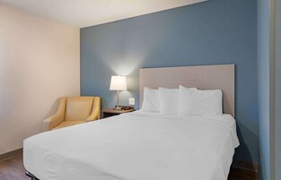 Una habitación de hotel con una cama grande, una lámpara de noche, una silla y una mesita de noche.