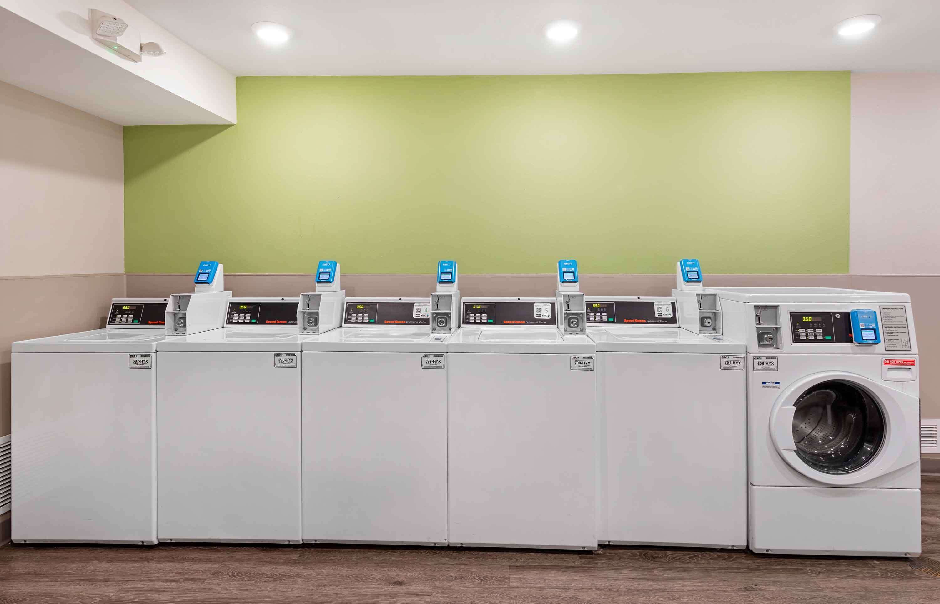 A row of white laundry machines with control panels and a single front-loading washing machine.