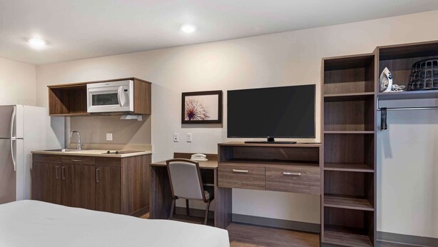 Habitación de hotel compacta con kitchenette, cama, escritorio y televisión.