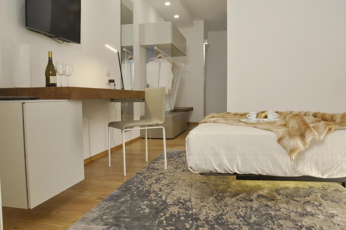 A modern hotel room with a bed, a desk, a chair, a TV, and a wardrobe.