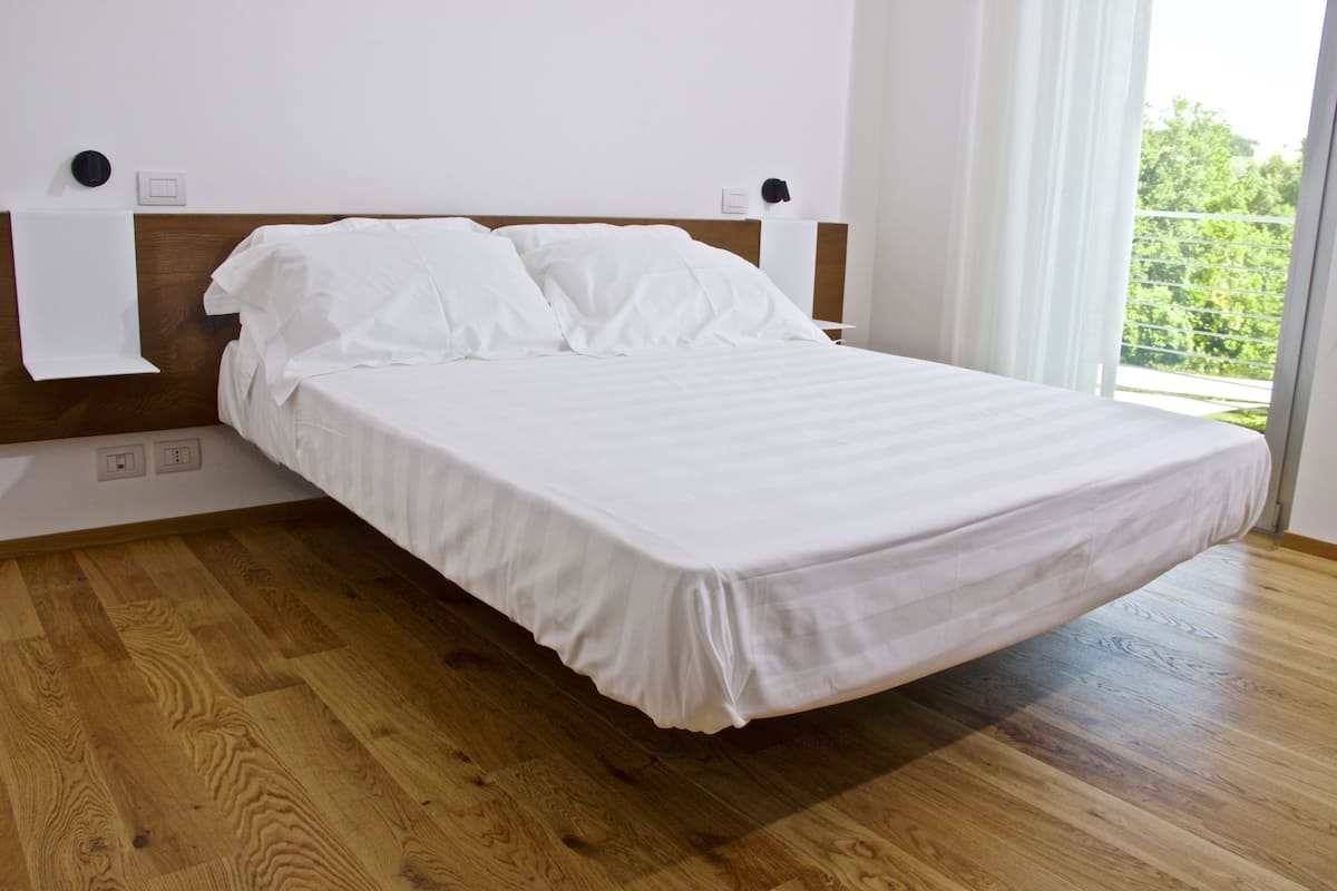 A single bed with a wooden headboard in a room with wooden flooring and a large window.