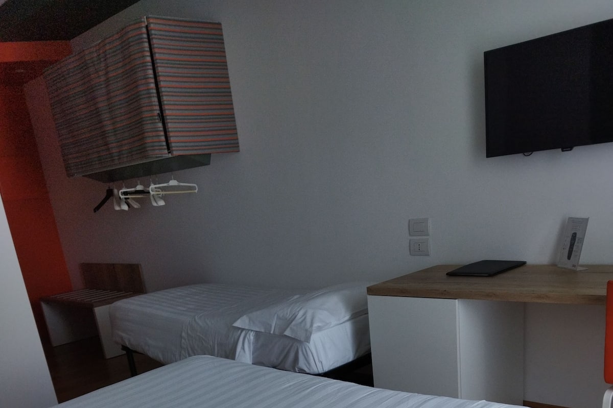 A hotel room with a large bed, a desk with a laptop, a TV mounted on the wall, and a striped curtain.
