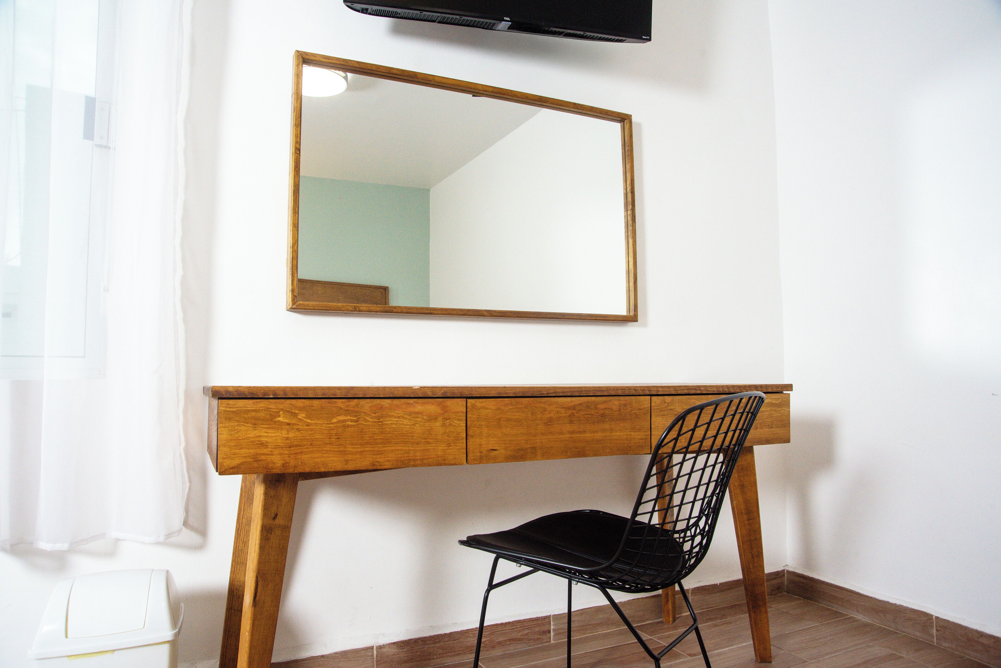 Un escritorio de madera con una silla negra, un espejo y un televisor montado en la pared.