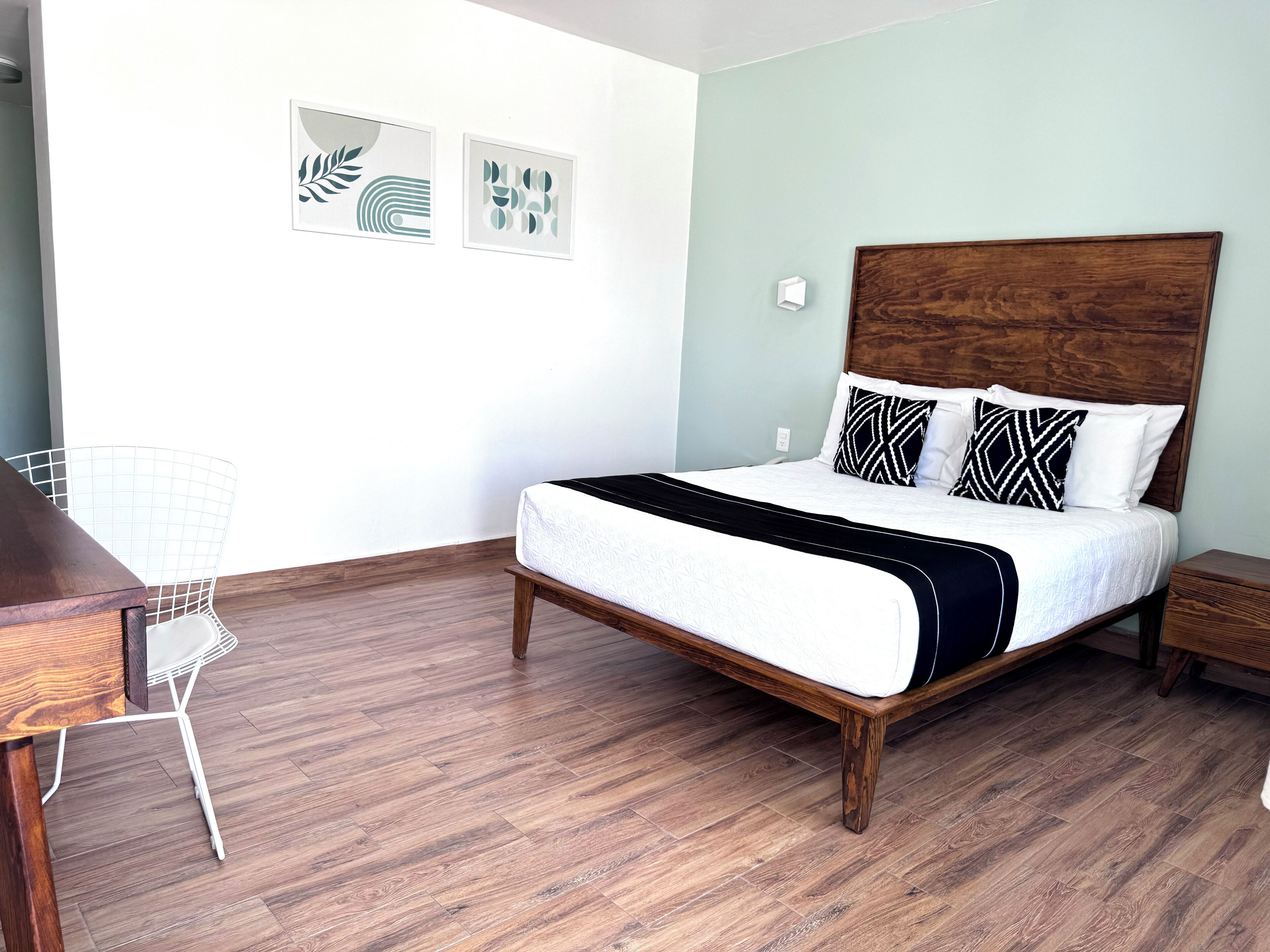Una camera da letto con un letto in legno, biancheria bianca, una sedia bianca e due quadri appesi al muro.