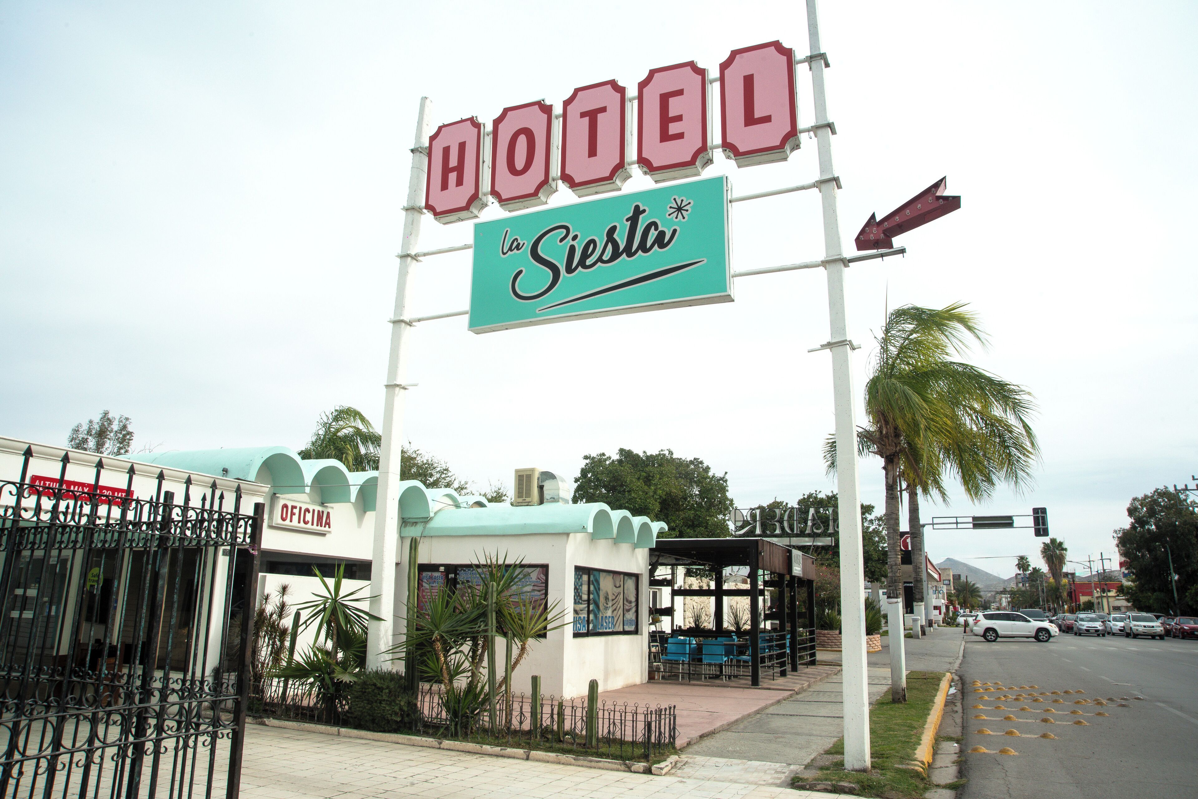 A hotel named "La Siesta" with a sign, a covered waiting area, and a fenced entrance.