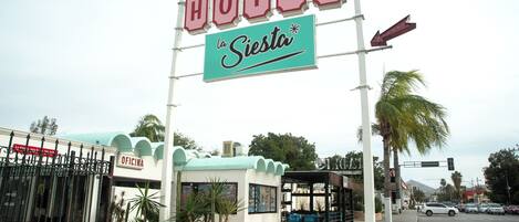 A hotel named "La Siesta" with a sign, a covered waiting area, and a fenced entrance.