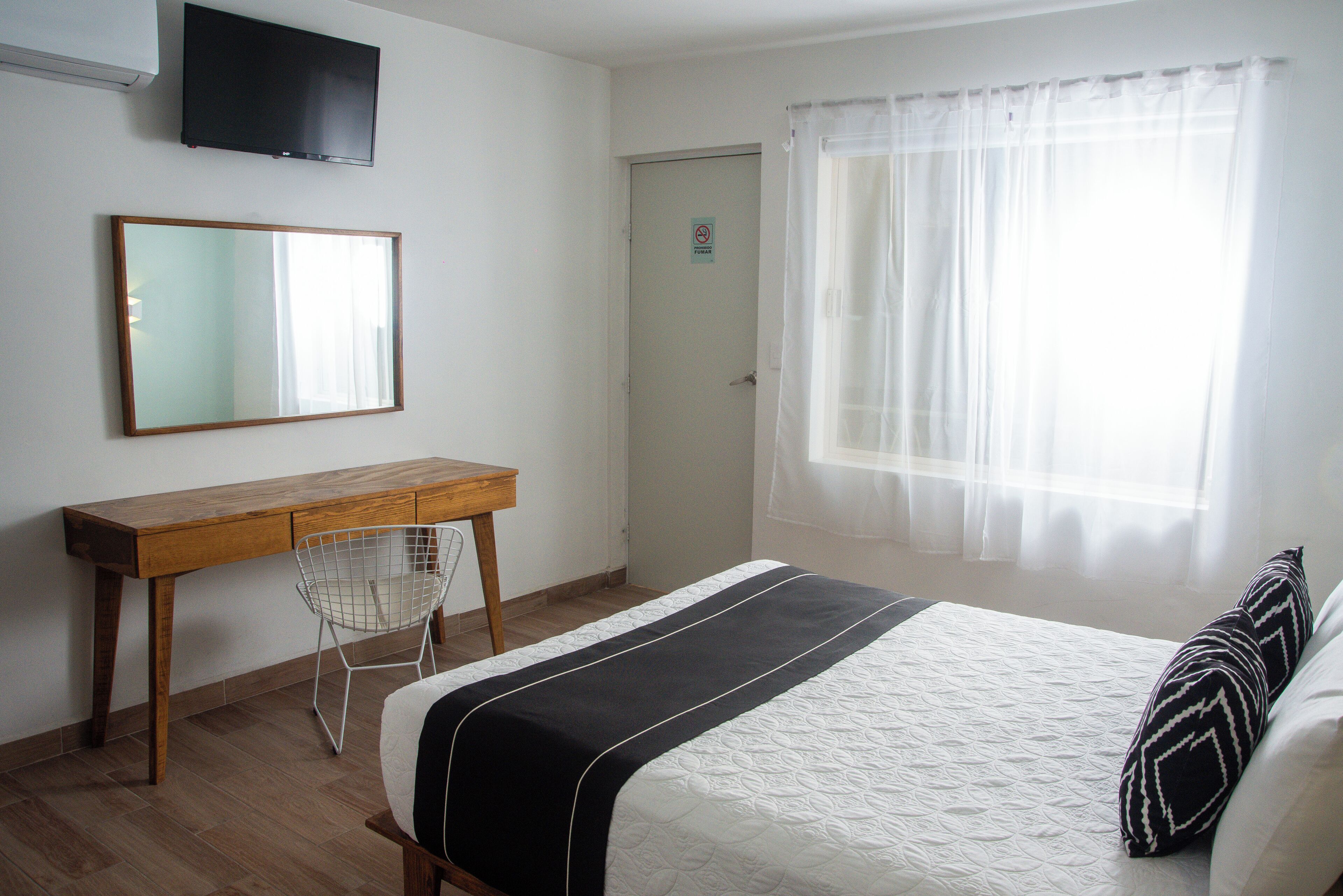 Un dormitorio con cama, escritorio, silla, televisor y ventana con cortinas.