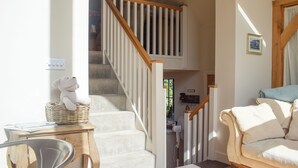 Un escalier avec des rampes en bois, un panier en osier, un canapé blanc et un tableau encadré au mur.