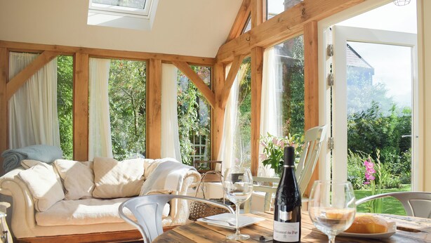 Une pièce chaleureuse avec un plafond en bois, de grandes fenêtres, un canapé, une table à manger et des verres à vin.