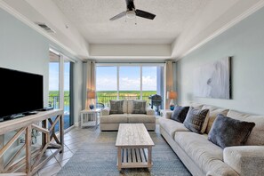 Ein geräumiges Wohnzimmer mit großem Fernseher, Deckenventilator, Sofa, Couchtisch und einem Balkon mit Blick.