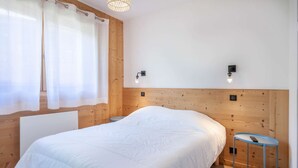 A bedroom with a wooden headboard, a bed with white bedding, a small round table, and two wall-mounted lights.