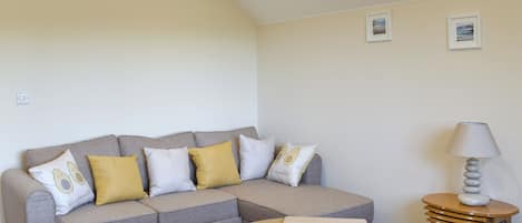 Una sala moderna con un sofá seccional gris, una mesa de centro redonda de madera y una pequeña mesita auxiliar con una lámpara.