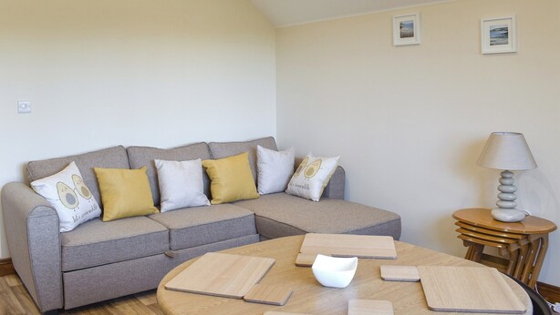 A modern living room with a grey sectional sofa, wooden coffee table, and a small side table with a lamp. - 2 bedroom accommodation in Sandown (Sandown)