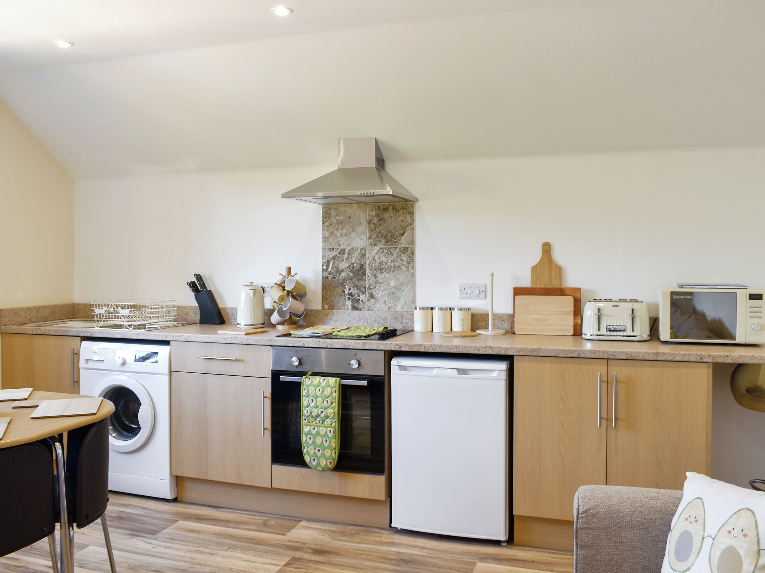 A kitchen with a washing machine, oven, microwave, and a wooden countertop.