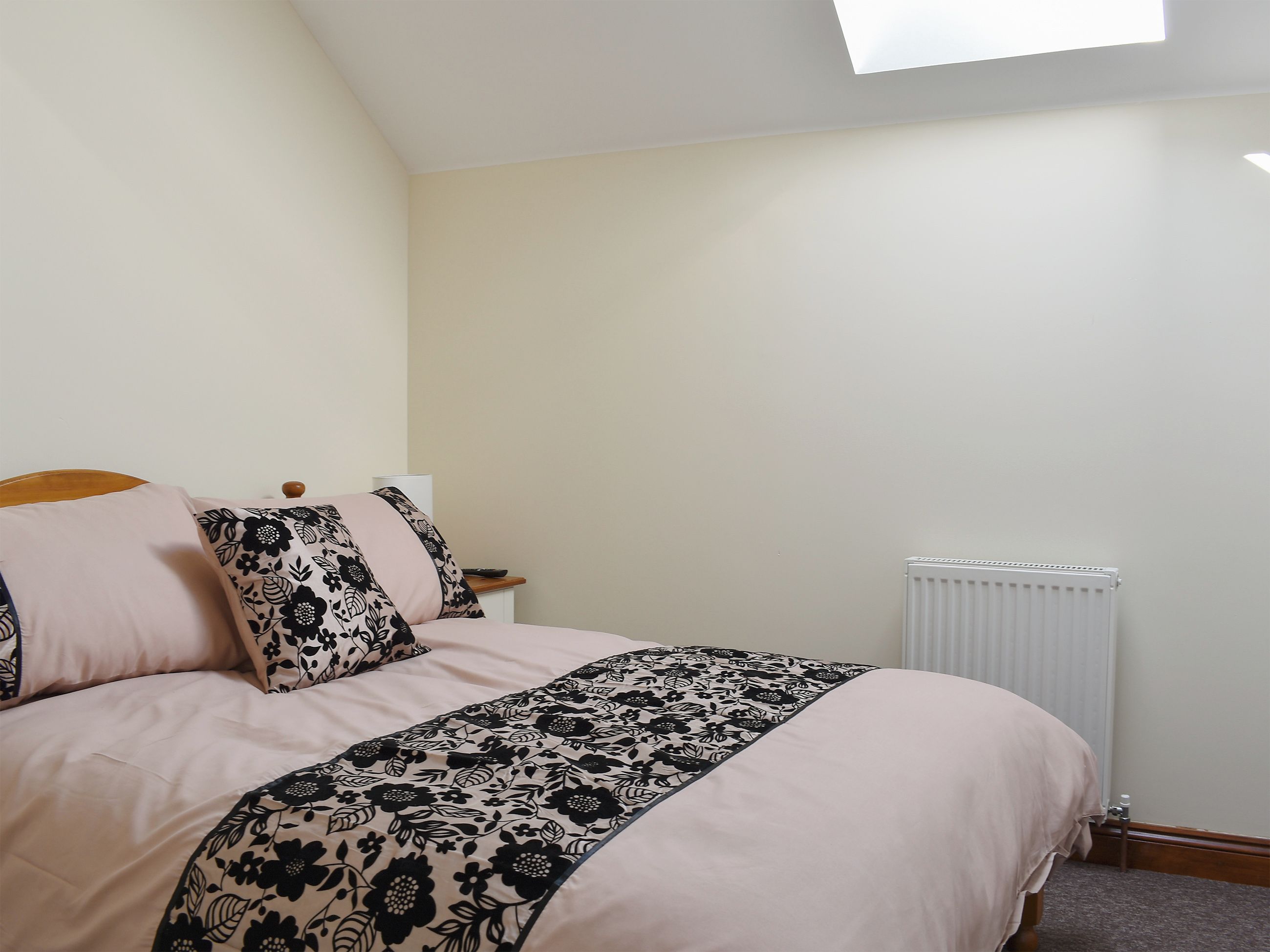 A bedroom with a bed, a nightstand, a radiator, and a window.
