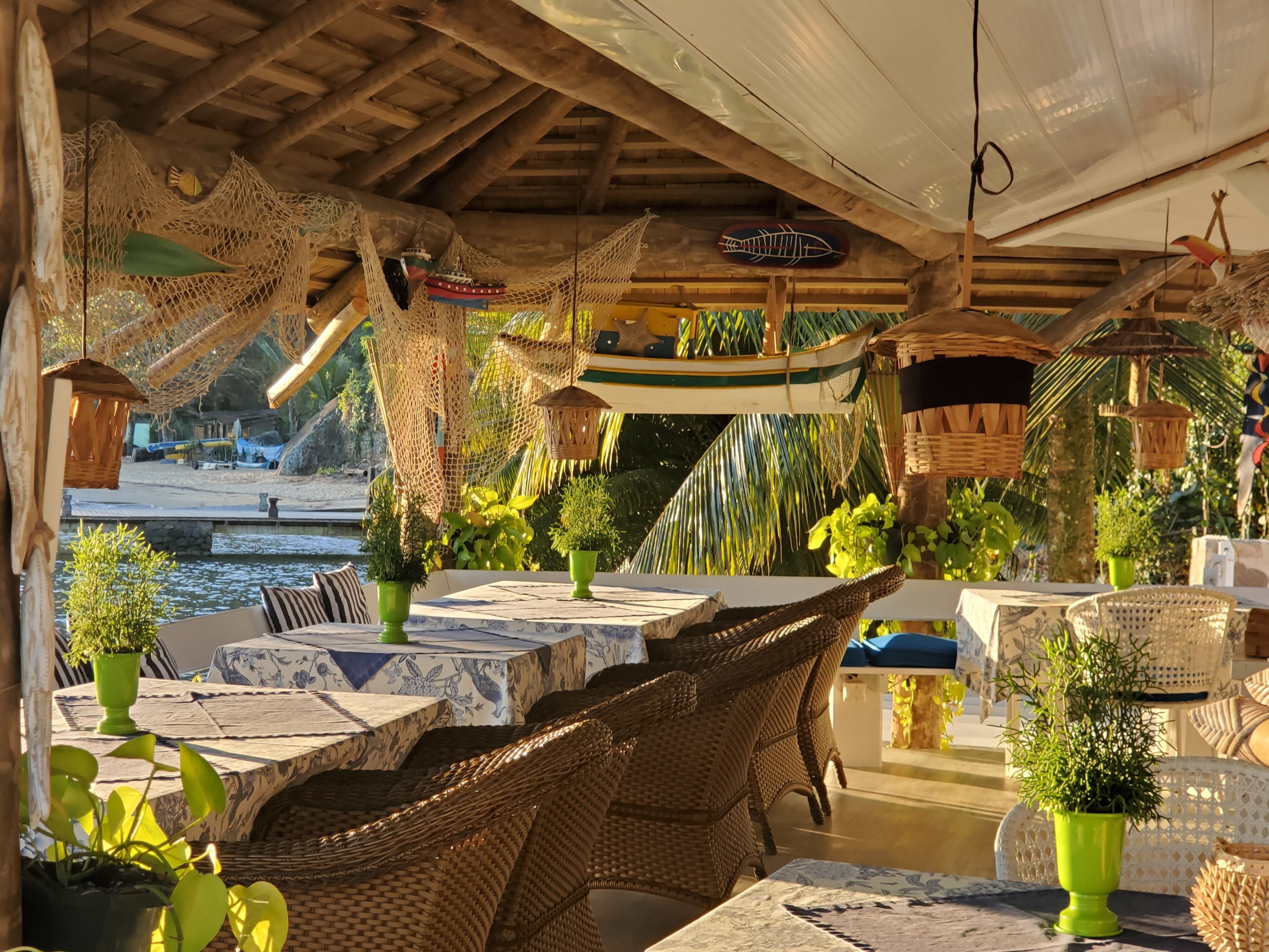 An outdoor dining area with wicker furniture, green potted plants, and a view of the water.