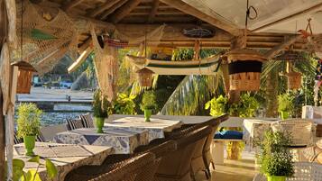An outdoor dining area with wicker furniture, green potted plants, and a view of the water.