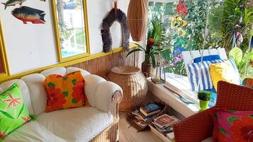 A cozy room with a white sofa, wicker furniture, and a window with a view of greenery.