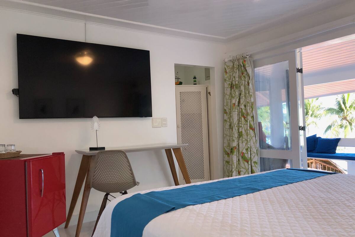 A hotel room with a bed, a desk, a TV, a wardrobe, and a view of the outdoors.