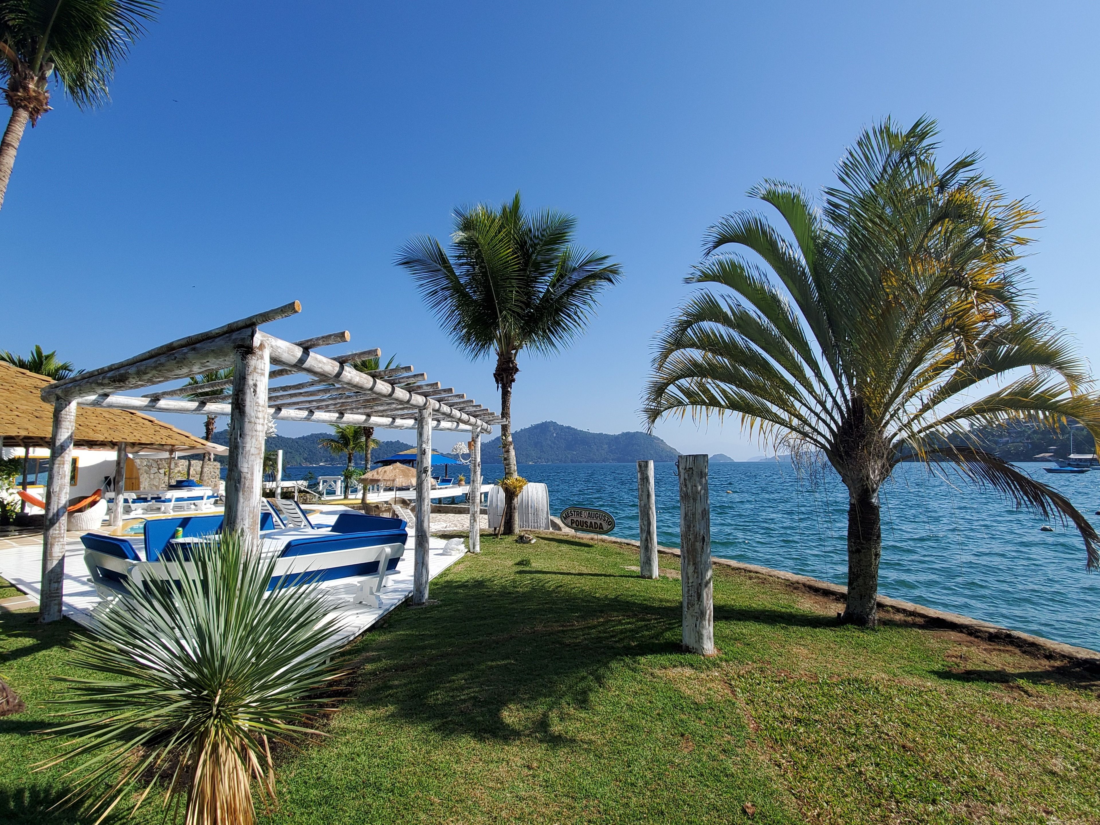 Zona sulla spiaggia con una pergola in legno, sedie a sdraio e una piscina.