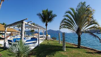 Zona sulla spiaggia con una pergola in legno, sedie a sdraio e una piscina.