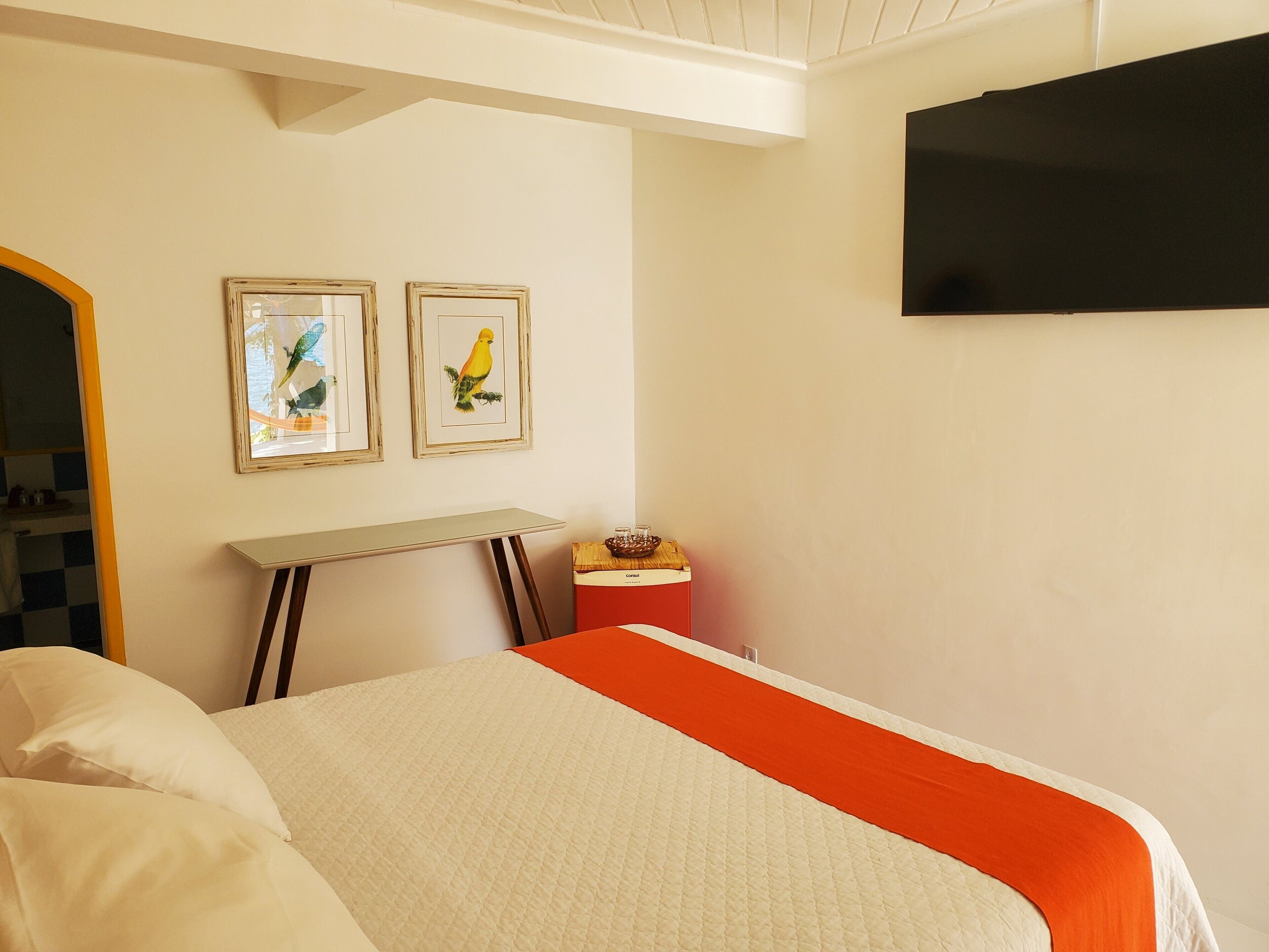 Ein Schlafzimmer mit einem Bett, einem Nachttisch, einem an der Wand montierten Fernseher und zwei gerahmten Bildern.