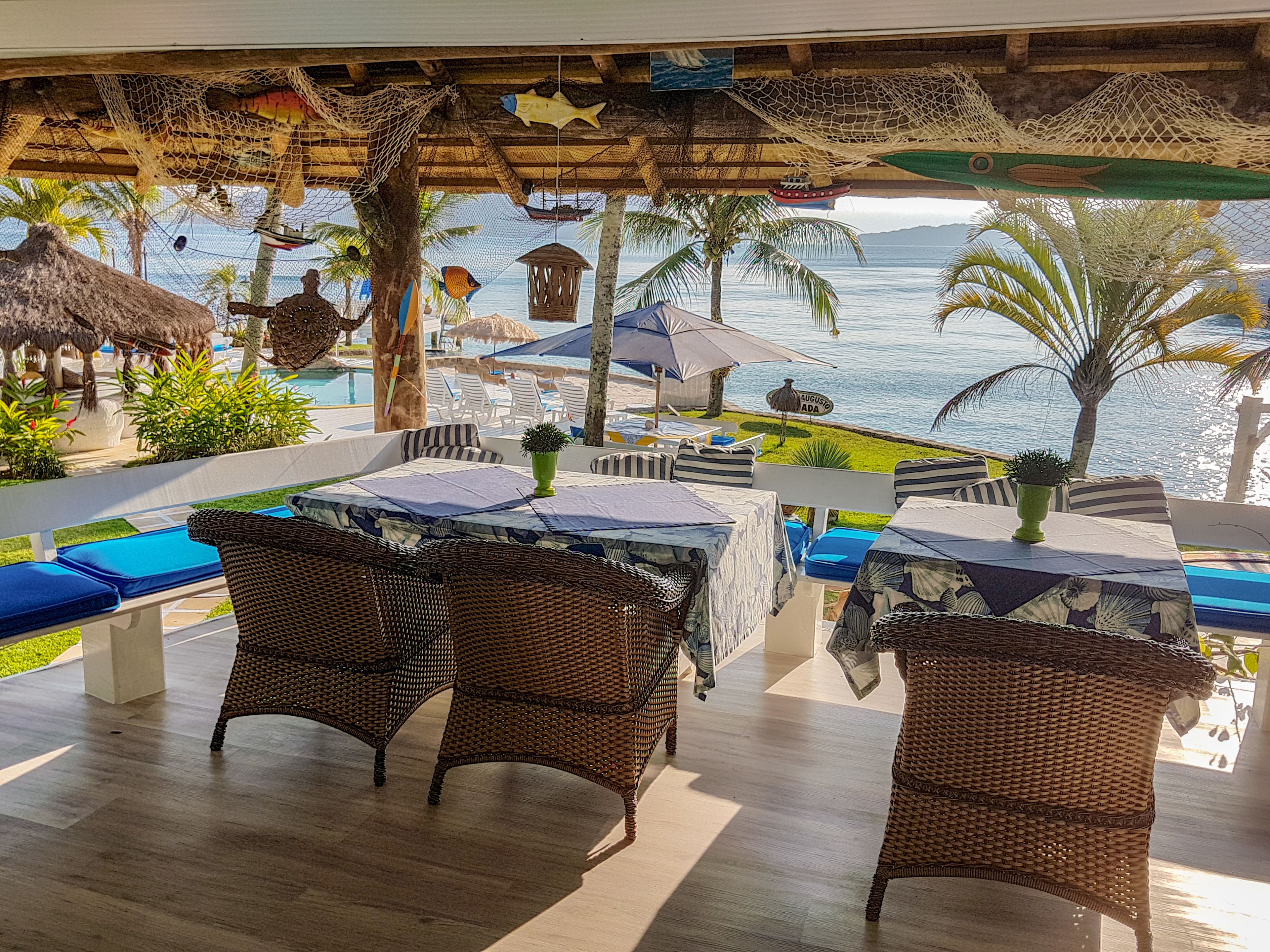An outdoor seating area with wicker furniture, umbrellas, and a view of the sea.