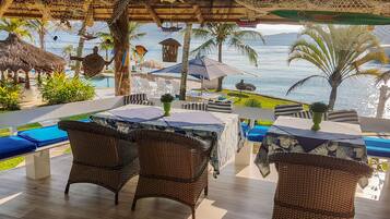 An outdoor seating area with wicker furniture, umbrellas, and a view of the sea.