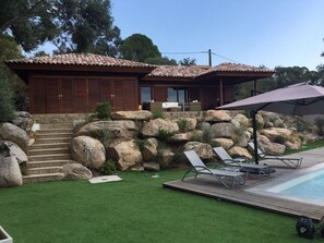 En villa med en stentrappa som leder upp till en träveranda, en swimmingpool och utomhusmöbler.