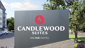 Señal de Candlewood Suites, un hotel IHG, con un logotipo rojo, rodeada por un jardín ajardinado con diversas flores de colores.