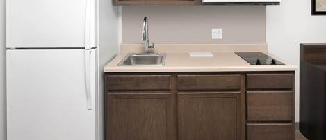 A compact kitchen with a white refrigerator, a microwave, a sink, and wooden cabinets.