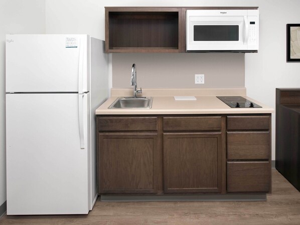 A compact kitchen with a white refrigerator, a microwave, a sink, and wooden cabinets.