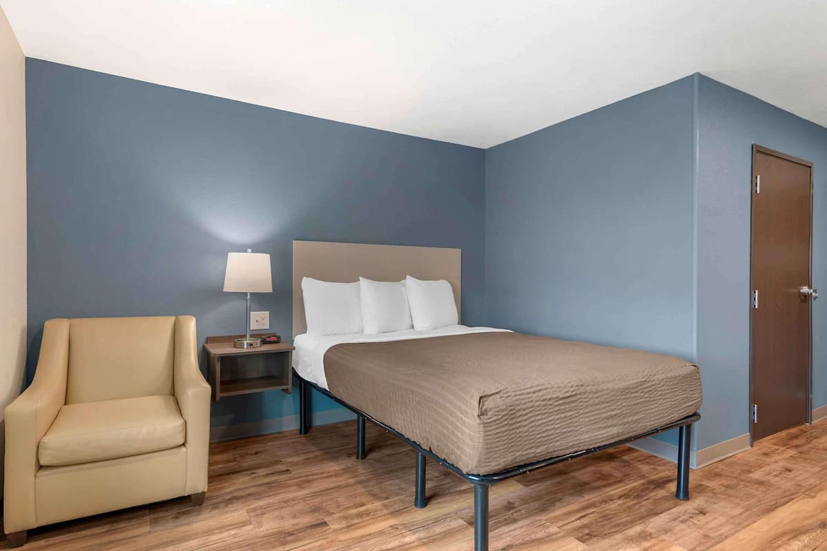 A bedroom with a bed, a chair, a nightstand, and a door.