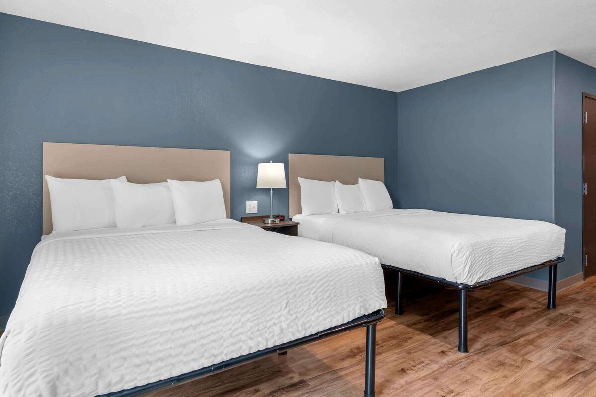 A hotel room with two beds, a nightstand with a lamp, and a wooden floor.